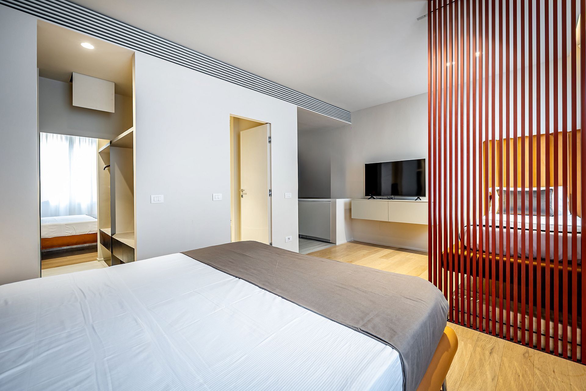 A modern hotel room with a bed, a TV, a desk, and a wardrobe.