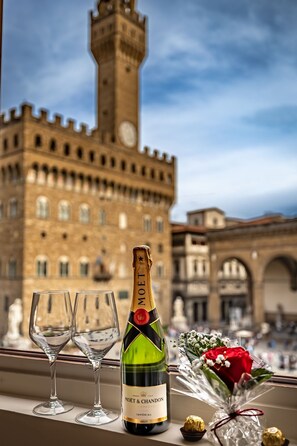 A bottle of Moët & Chandon champagne, two empty glasses, a bouquet of flowers, and a chocolate truffle on a window ledge with a historic building in the background. - Signoria Collection (Florence)