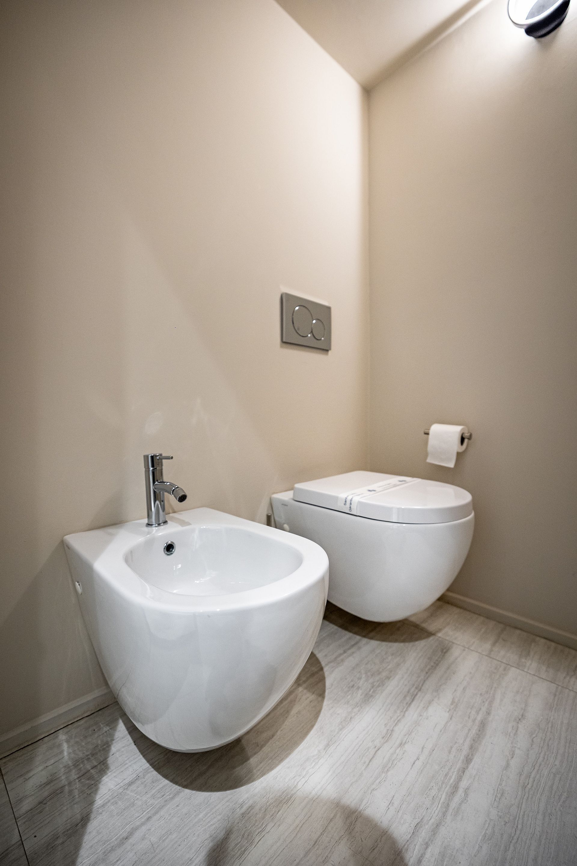 A modern bathroom with a bidet, a toilet, and a wall-mounted light fixture.
