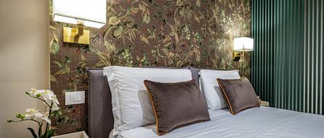 A hotel room with a bed, two wall-mounted lamps, a floral wallpaper, and a nightstand with a plant.