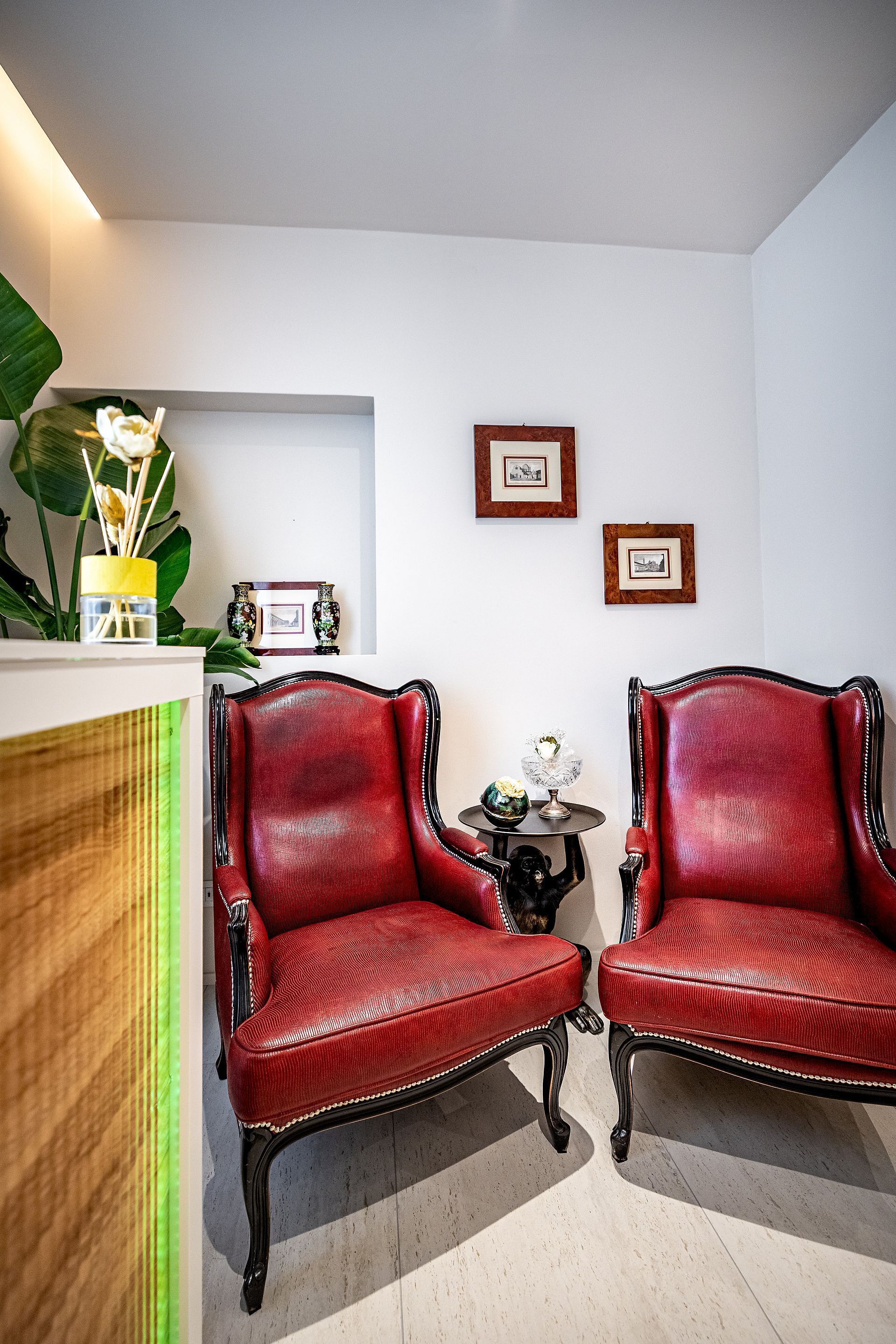 Ein Zimmer mit zwei roten Ledersesseln, einem kleinen Tisch mit einer Vase und gerahmten Bildern an der Wand.