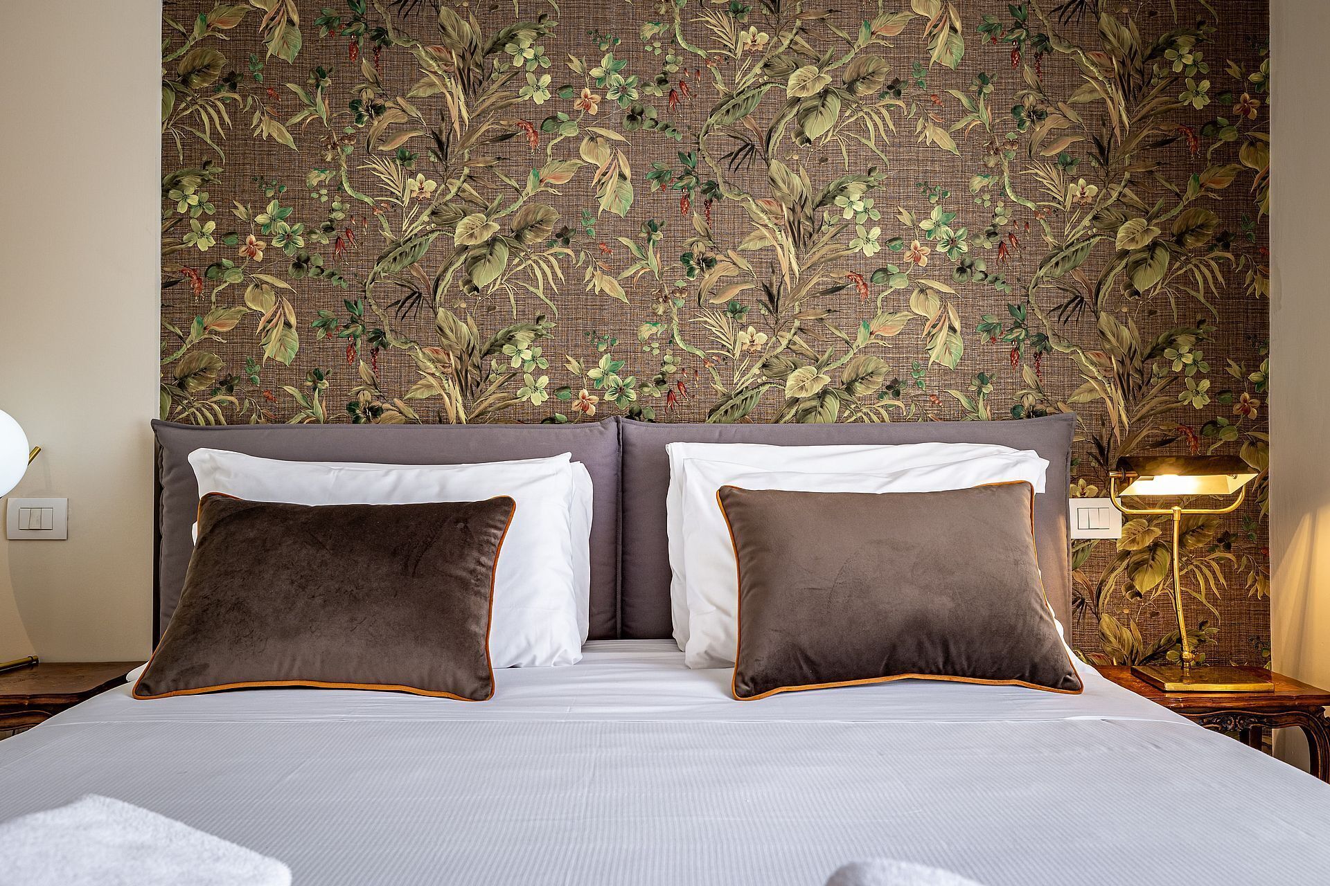 A neatly made bed with two pillows, a headboard with a floral pattern, and a bedside lamp.