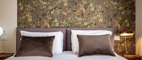 A neatly made bed with two pillows, a headboard with a floral pattern, and a bedside lamp.