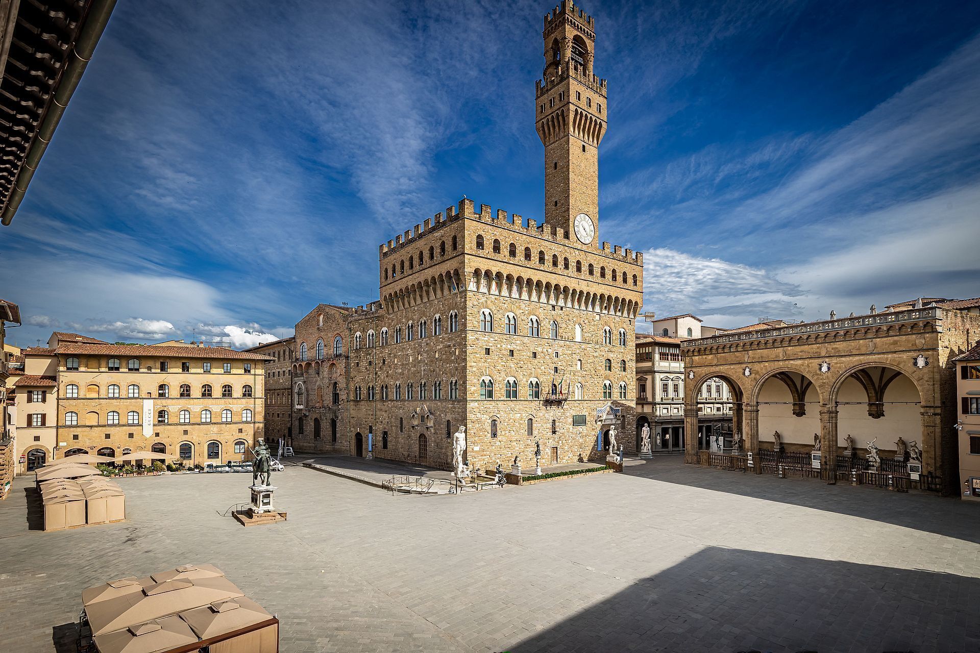 A historic square with a prominent tower, a statue, and traditional buildings.