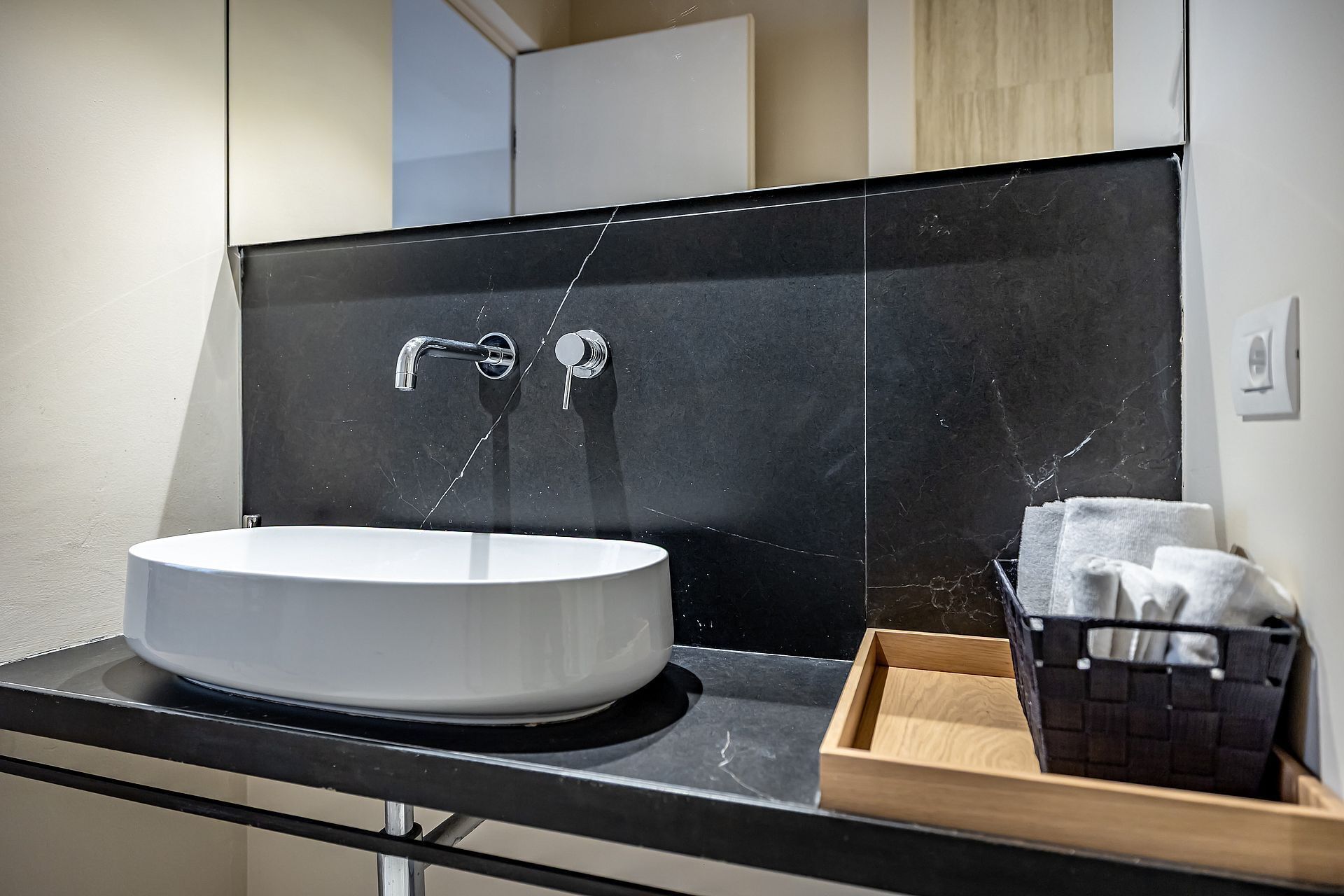 Ein Badezimmer mit einem weißen Waschbecken, einer schwarzen Fliesenspiegel und einer Holztablett mit Handtüchern.