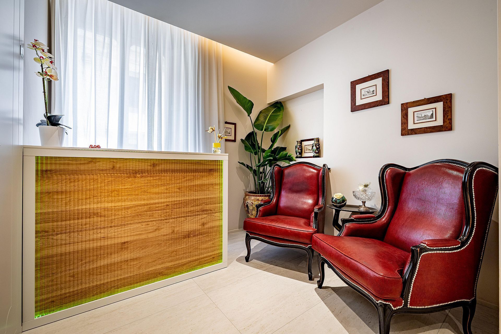 A room with a reception desk, two red leather chairs, a large plant, and framed pictures on the wall.