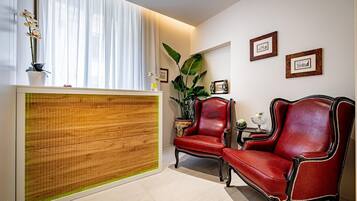 A room with a reception desk, two red leather chairs, a large plant, and framed pictures on the wall.