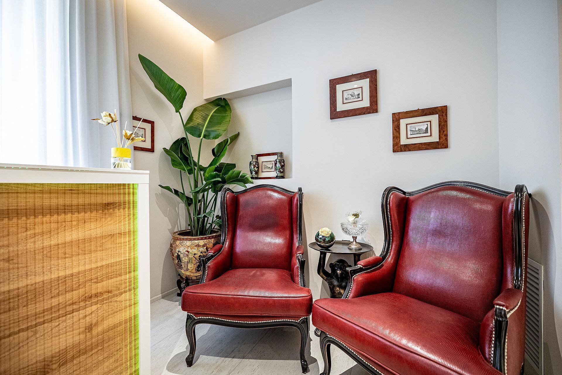 A room with two red leather chairs, a large potted plant, framed pictures on the wall, and a wooden cabinet.
