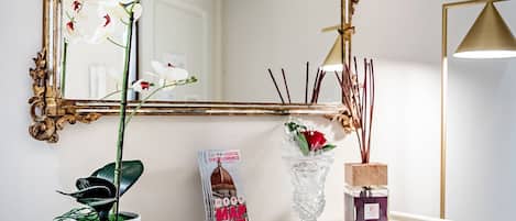 A white dresser with a mirror, a potted plant, a vase with flowers, and a candle.