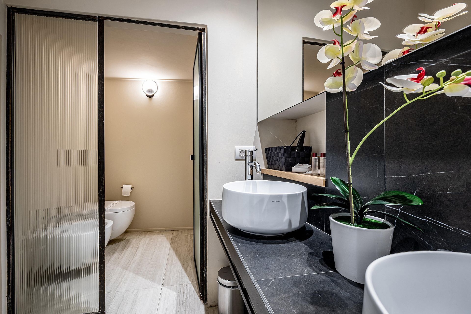 Ein modernes Badezimmer mit Toilette, einem weißen Waschbecken, einem Spiegel und einer Orchidee im Topf.