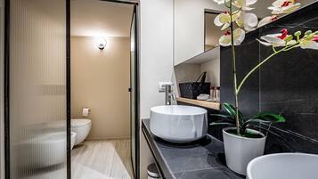 Ein modernes Badezimmer mit Toilette, einem weißen Waschbecken, einem Spiegel und einer Orchidee im Topf.