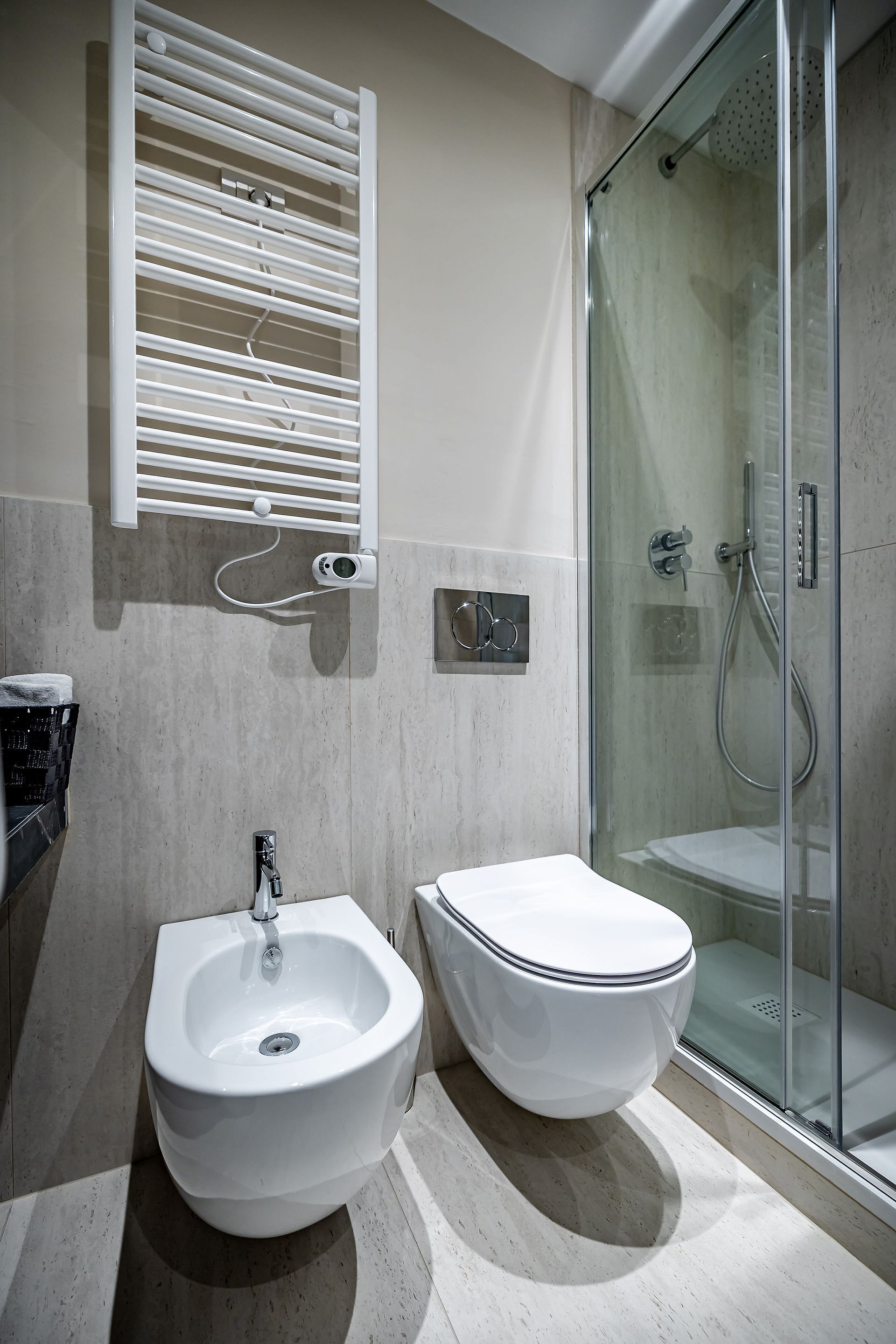 A modern bathroom with a bidet, a toilet, a glass shower enclosure, and a towel rack.