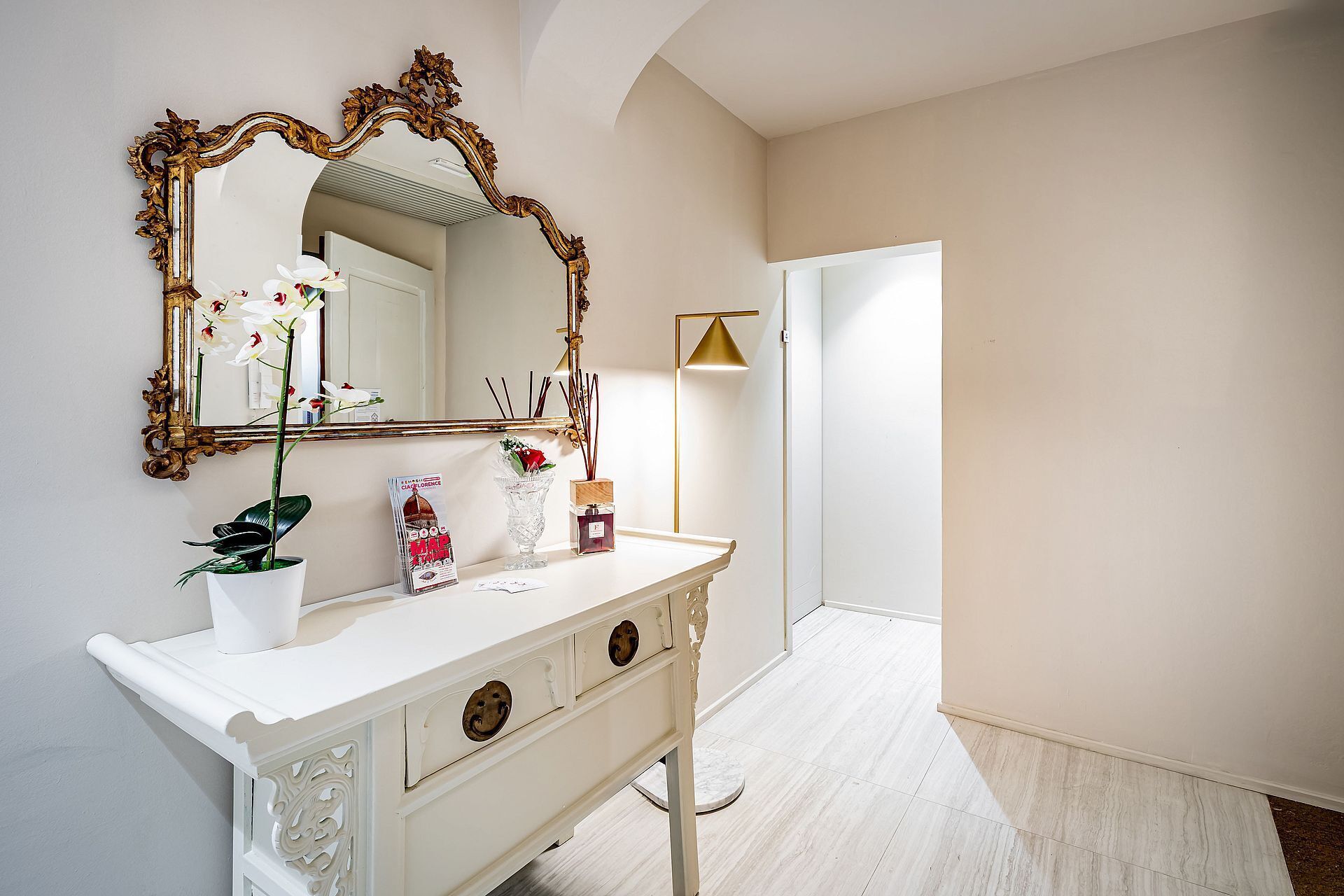 A white vanity with a large ornate mirror, a potted plant, and a magazine on the counter.