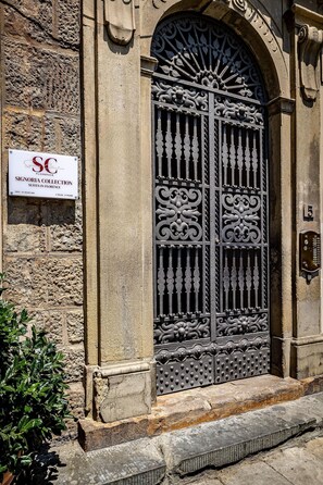 A stone building with a wrought iron gate, a sign for Signoria Collection Suites in Florence, and a number plaque. - Signoria Collection (Florence)