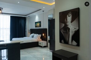 A modern hotel room with a bed, bedside table, nightstand, and a large framed picture on the wall. - Cozy Studio apartment (Accra)