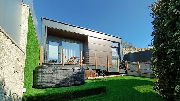 A modern house with a large glass door, a small outdoor seating area, and a stone wall.