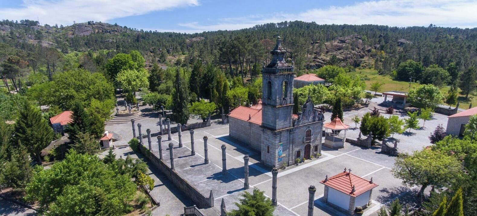 Une église dotée d’un clocher, entourée d’arbres et située dans un paysage vallonné.