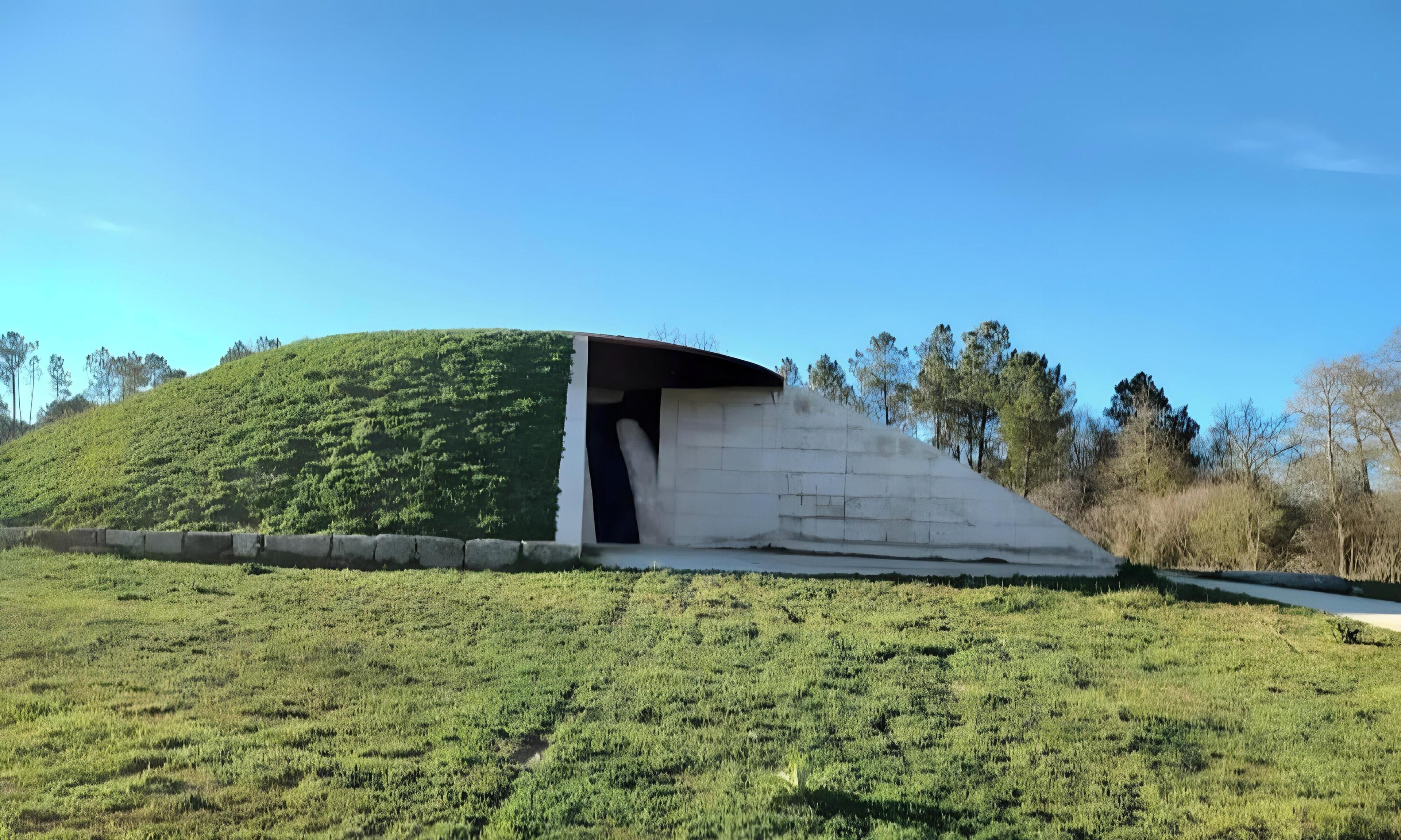 A mound with a covered entrance, surrounded by a grassy field and trees.