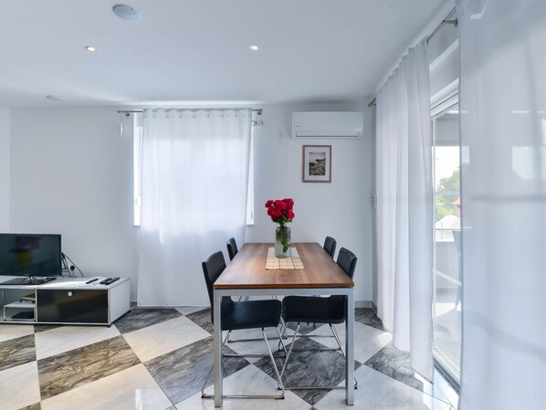 Ein moderner Essbereich mit einem Holztisch, schwarzen Stühlen, einem Fernseher und einer Vase mit roten Blumen.