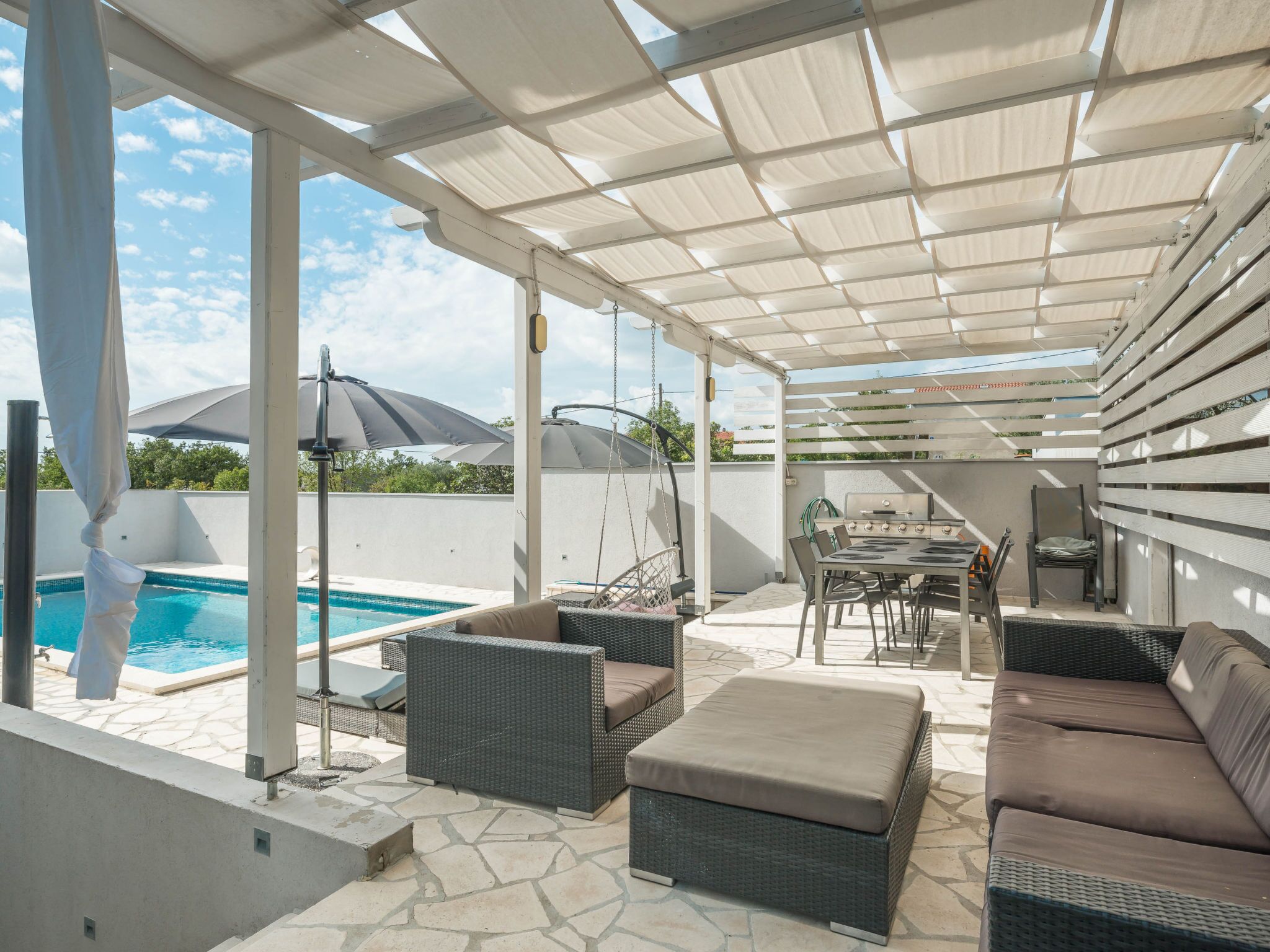 An outdoor patio with a pool, wicker furniture, and a grill area.