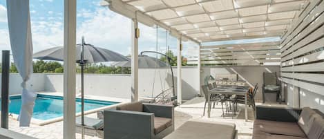 An outdoor patio with a pool, wicker furniture, and a grill area.