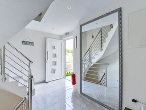 Ein modernes Interieur mit einem großen Spiegel, der eine Treppe reflektiert, einer Tür mit einem kleinen Fenster und einem Feuerlöscher auf dem Boden.