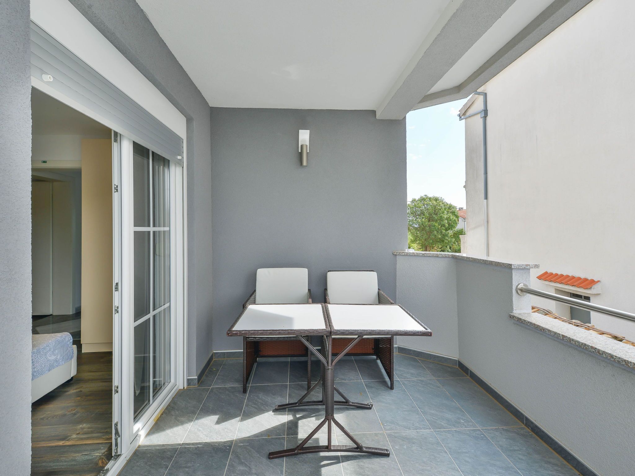 A balcony with a table and chairs, a sliding glass door, and a view of the outside.