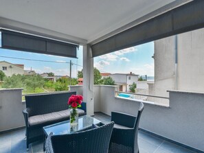 Ein Balkon mit Glastisch, Korbstühlen und einem Blumenstrauß.