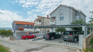 Un edificio residencial con área de estacionamiento techada, un coche rojo y un coche negro estacionados al frente.