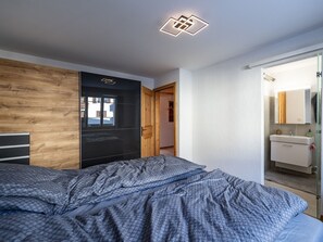 Ein modernes Schlafzimmer mit Bett, Holzvertäfelung, einem schwarzen Kleiderschrank und einem durchgehenden Türrahmen einsehbaren Badezimmer.