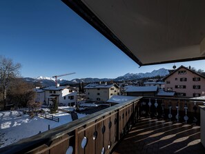 Un balcon donnant sur une ville et des montagnes enneigées.