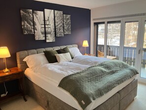 A bedroom with a large bed, two bedside lamps, a view of the outdoors through a sliding glass door, and three wall-mounted artworks. - Baumann Laax Riva, (Laax GR), by Interhome (Laax)