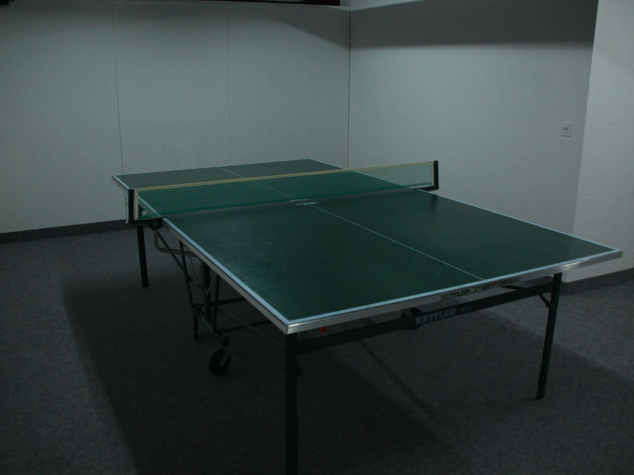 A table tennis table in a room with a carpeted floor and plain walls.
