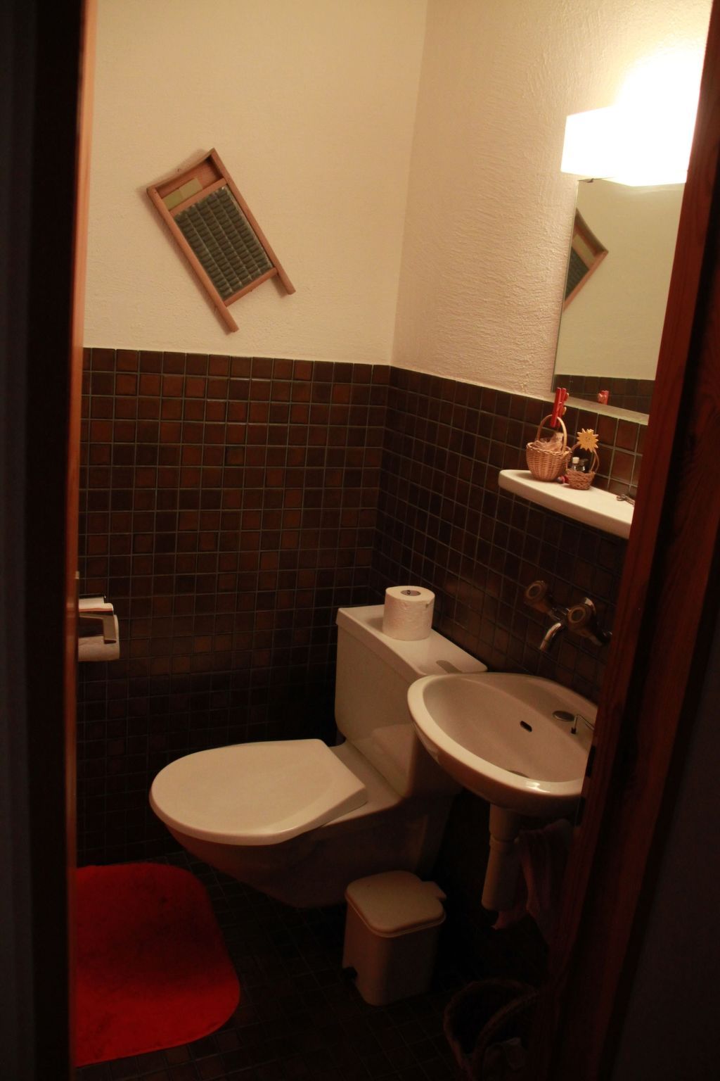 A small bathroom with a toilet, sink, and a red mat on the floor.