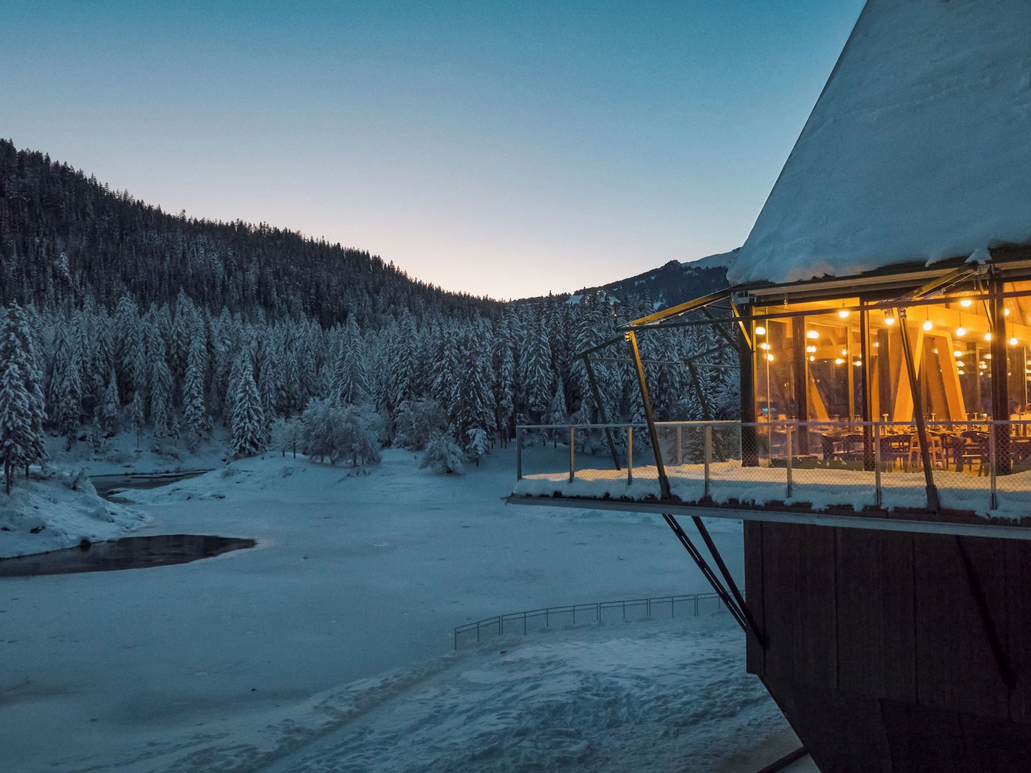 A snow-covered landscape with a building featuring a glass enclosure and interior lighting.