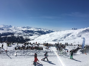 A snowy ski slope with skiers and a clear view of snow-covered mountains.