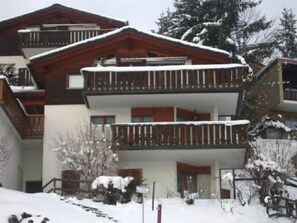 Ein mehrstöckiges Gebäude mit Balkonen, umgeben von schneebedeckten Bäumen.