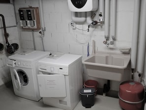 Ein Waschraum mit zwei Waschmaschinen, einem Waschbecken und einem roten Warmwasserbereiter.