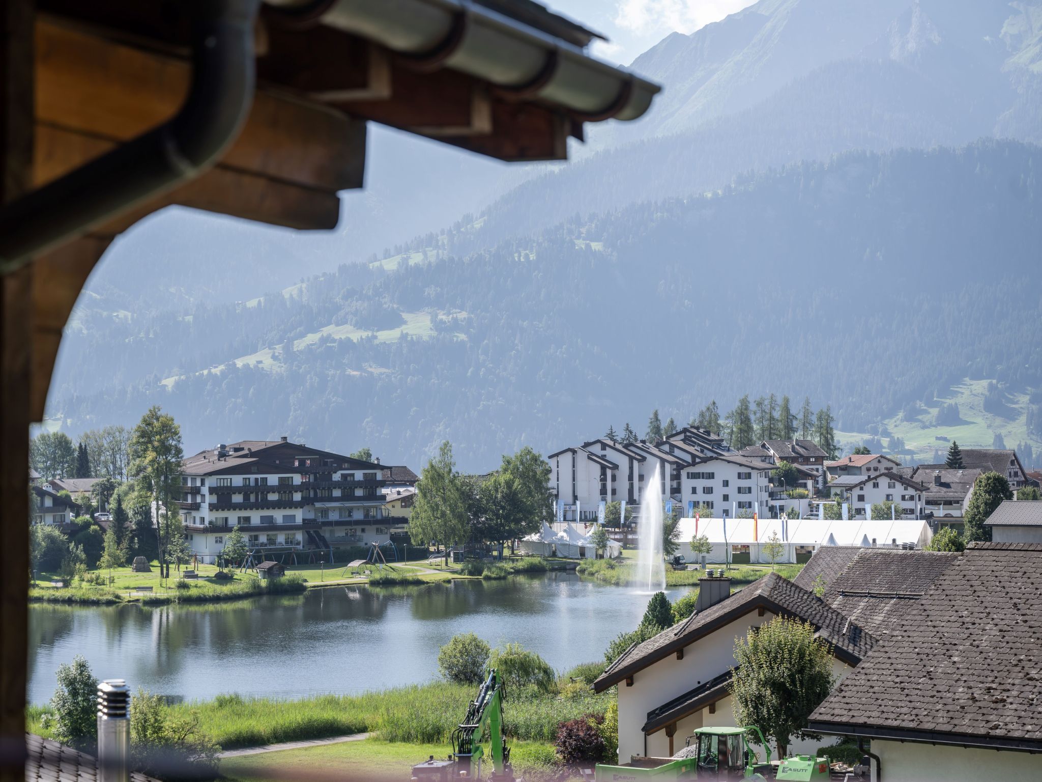 A lakeside view of a mountain town with buildings, a fountain, and a clear sky.
