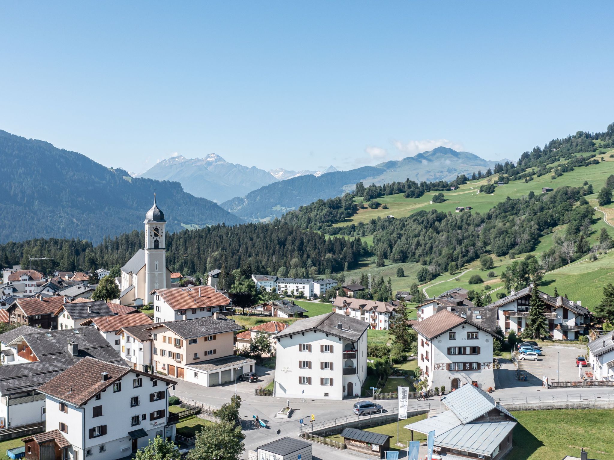 Eine Stadt mit einem markanten Kirchturm, umgeben von Wohnhäusern und saftig grünen Hügeln.
