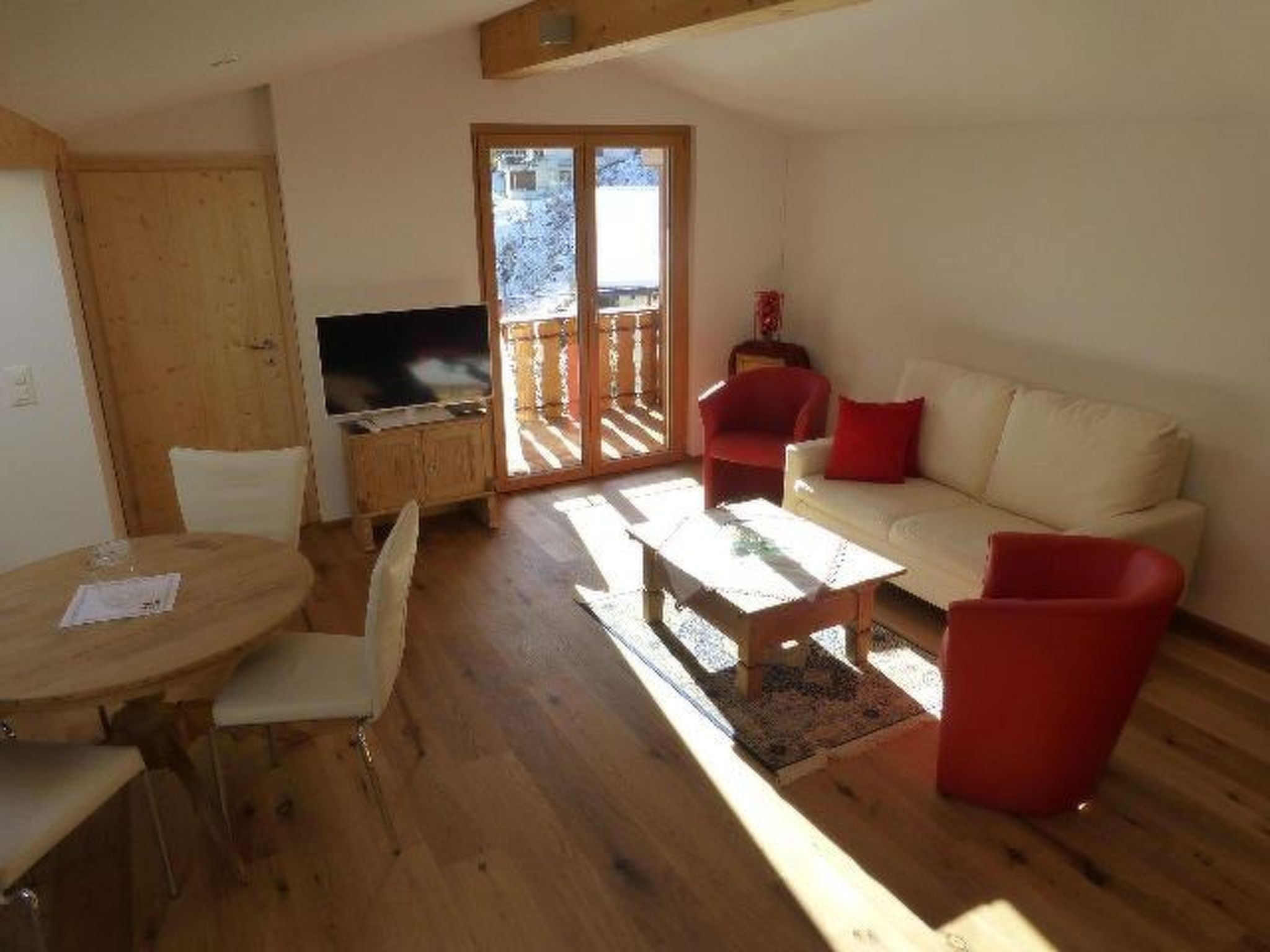 A living room with a sofa, a coffee table, a TV, and a dining area with chairs and a table.
