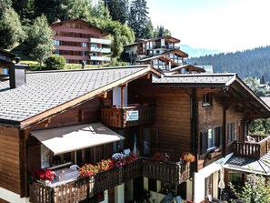 A wooden chalet with a balcony, a covered outdoor seating area, and a view of the surrounding forest and mountains. - Casa Ual / Capaul, (Laax Dorf), 332 by Interhome (Laax)