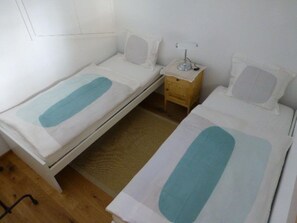 A room with two single beds, a small wooden nightstand with a lamp, and a woven mat on the floor. - Casa Ual / Capaul, (Laax Dorf), 332 by Interhome (Laax)