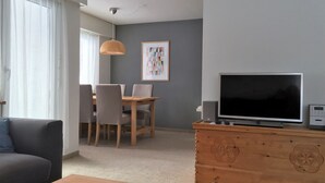 Una sala de estar con televisor, un mueble de madera, una mesa de comedor con sillas y un sofá.