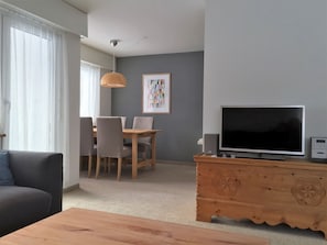 A living room with a television, a wooden cabinet, a dining table with chairs, and a sofa. - Haus Beta / Meier, (Flims Waldhaus), 48 by Interhome (Flims)