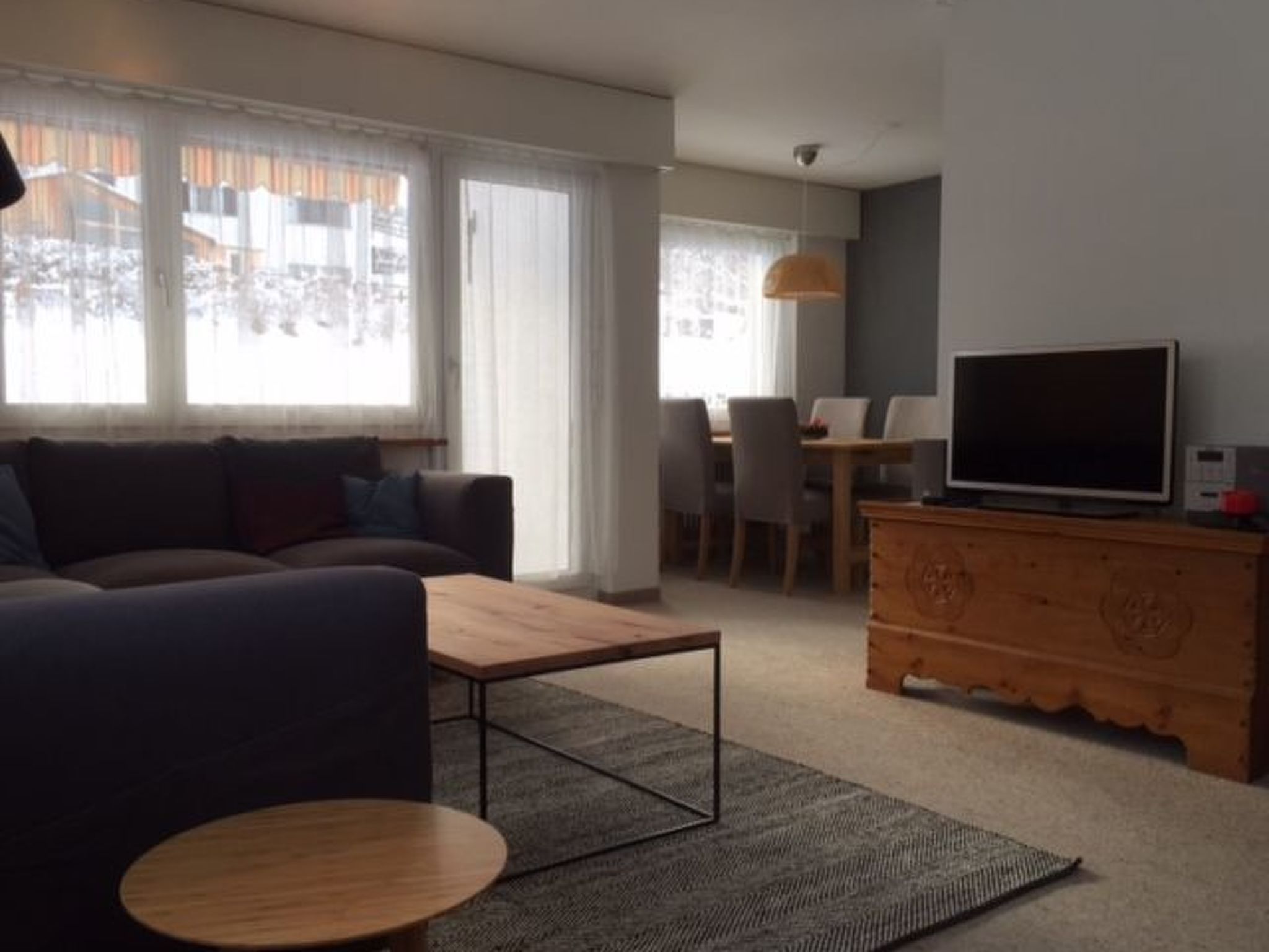 A modern living room with a sofa, coffee table, TV, and a dining area with chairs and a table.
