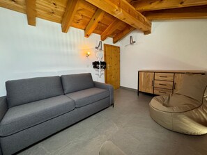 A room with a grey sofa, a wooden cabinet, and a beige bean bag chair. - Alpenbijou "CASA BIALA", (Laax GR), by Interhome (Laax)
