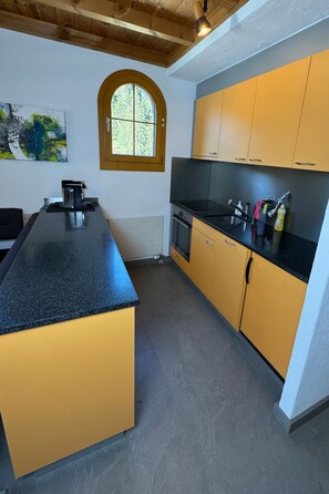 A kitchen with a central island, a window, and a painting on the wall. - Alpenbijou "CASA BIALA", (Laax GR), by Interhome (Laax)