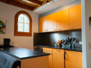 A kitchen with a black countertop, orange cabinets, a window, and a coffee machine. - Alpenbijou "CASA BIALA", (Laax GR), by Interhome (Laax)