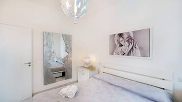 Quarto com cama, mesa de cabeceira, abajur, espelho e duas obras de arte emolduradas na parede.